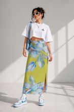 Load image into Gallery viewer, Woman wearing a white crop top and floral skirt with sneakers, standing against a light background.