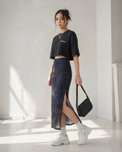 Load image into Gallery viewer, Woman wearing a black crop top and dark blue patterned skirt in a bright room.