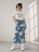 Load image into Gallery viewer, Woman wearing a white graphic t-shirt and blue floral skirt in a bright room.