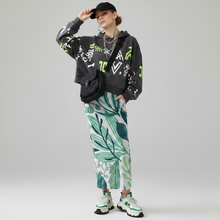 Load image into Gallery viewer, Person wearing a black hoodie with colorful designs, a green leaf-patterned pencil skirt, and white sneakers on a gray background
