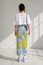 Load image into Gallery viewer, Person wearing a white crop top and colorful floral skirt in a bright room.
