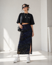 Load image into Gallery viewer, Woman wearing a black crop top and patterned skirt in a bright room.
