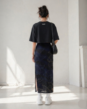 Load image into Gallery viewer, Person wearing a black t-shirt and dark floral skirt in a minimalistic room.
